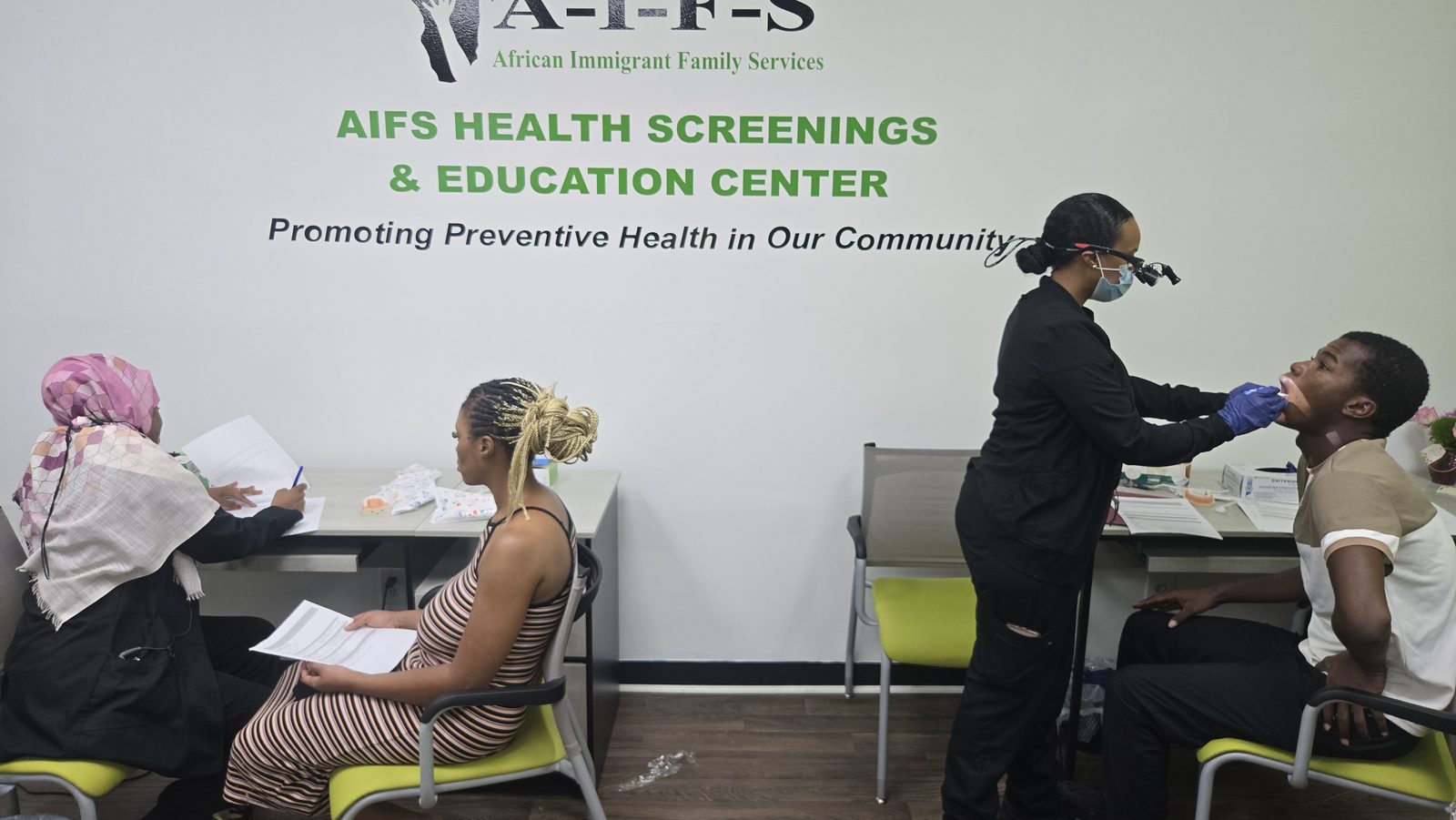 A healthcare worker uses a swab near a seated person’s mouth at a screening table.