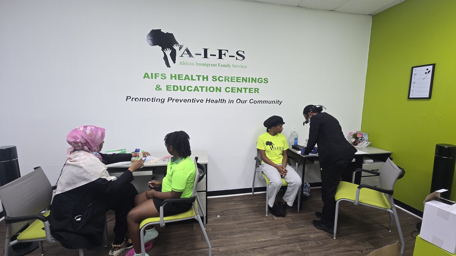 A room with tables where adults take part in a screening activity beneath AIFS signage.