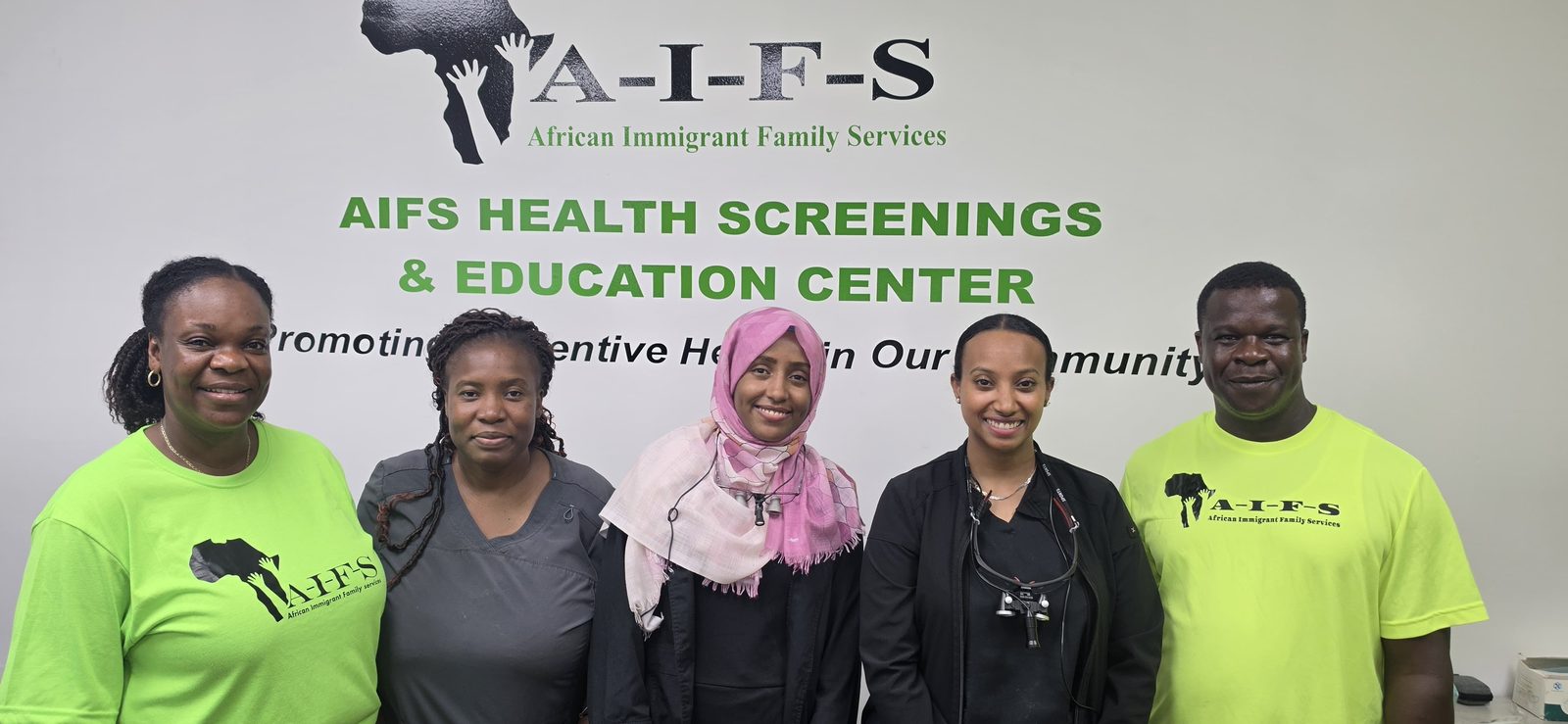 Five people stand together in front of an AIFS Health Screenings and Education Center wall sign.